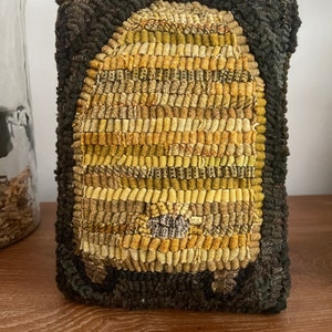 May include: A brown and yellow hand-stitched beehive pillow with a dark brown border.