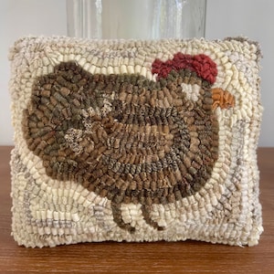 May include: A brown and white hand-stitched pillow with a brown chicken design. The chicken has a red comb and a white background.