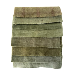 May include: A stack of eight rectangular fabric swatches in various shades of green. The top swatch features a brown plaid pattern, while the others display solid tones ranging from light sage to deep olive, all with a soft, textured, felted surface.