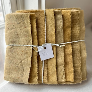 Puede incluir: Un paquete de ocho muestras de tela en varios tonos de marrón claro, atadas con una cuerda y etiquetadas como "Tan".