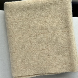 May include: A cream-colored, soft, fuzzy fabric swatch. The fabric has a slightly textured surface.