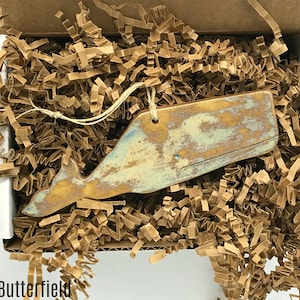 May include: A ceramic whale ornament in a light brown box with brown packing paper. The whale is painted in shades of blue, green, and gold, with a distressed finish.