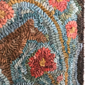 May include: Close-up of a colorful hooked rug with a circular pattern of red, brown, and blue yarn. The rug has a textured, hand-crafted look.