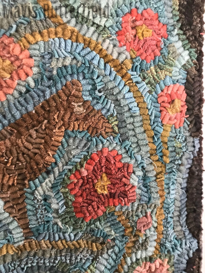 May include: Close-up of a colorful hooked rug with a circular pattern of red, brown, and blue yarn. The rug has a textured, hand-crafted look.