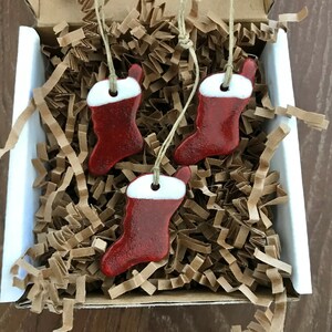May include: Three red and white ceramic Christmas stocking ornaments with white trim and a loop for hanging.