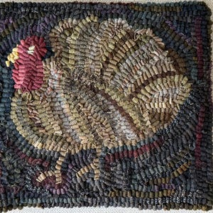 May include: Hand-hooked rug featuring a turkey design. The turkey has a red head and a fan of brown, tan, and green feathers. The background is dark blue with accents of purple and red. The rug is square and has a textured appearance.