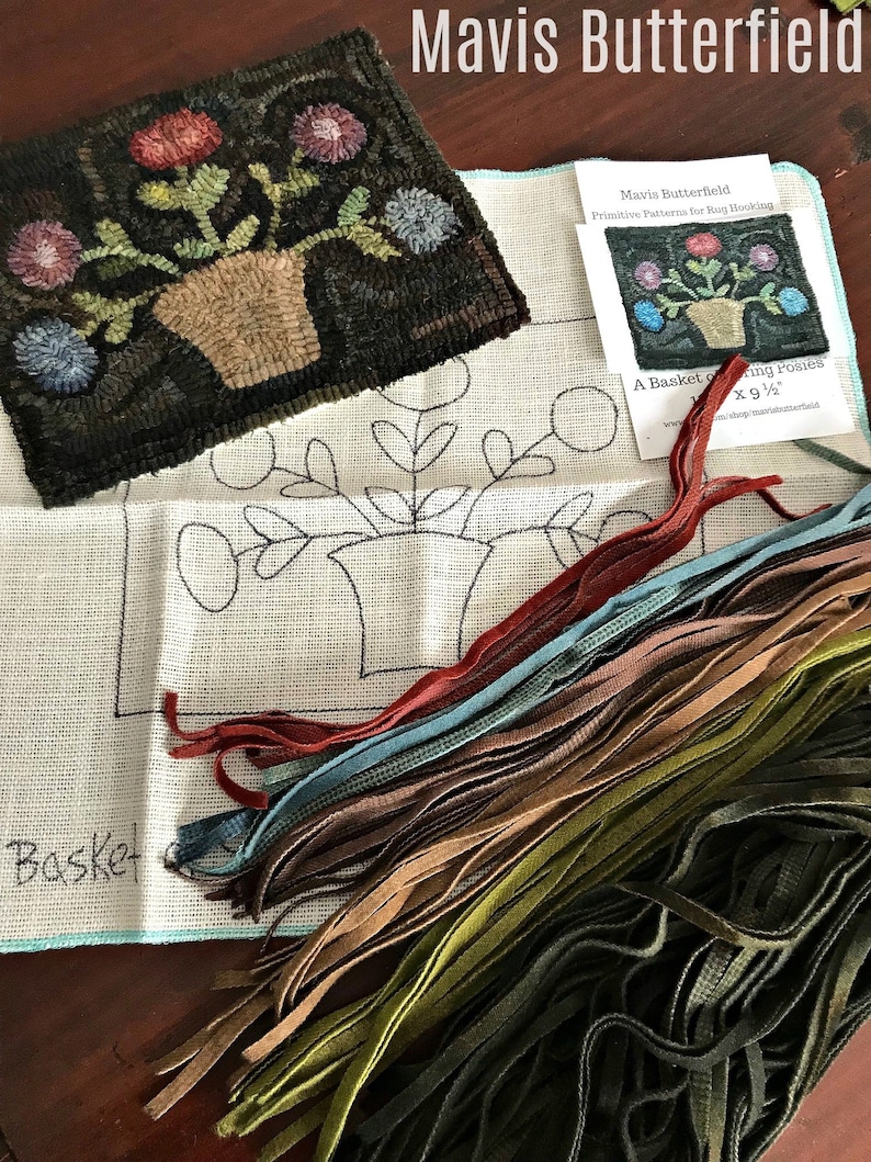 Op de afbeelding: Een close-up van een tapijt haakset met een gedrukt patroon voor een mand met bloemen. De set bevat een stuk canvas, garen en instructies. Het patroon is getiteld "A Basket of Blooming Posies" door Mavis Butterfield.