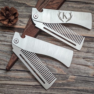 May include: Two silver folding combs with bottle opener features are displayed on a wooden surface. One comb has the letter "K" with antlers engraved on it. A pinecone sits in the background.