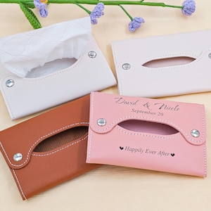 May include: Four leather tissue box covers in white, brown, and pink. One white cover is open, revealing tissues. The pink cover is inscribed with "David & Nicole, September 20" and "Happily Ever After."