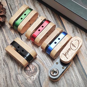 May include: Wooden and metal accessories with various colored accents, including green, red, blue, and black. One piece has the name "David" engraved on it. The items are arranged on a wooden surface.