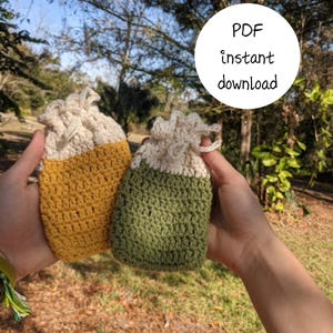 May include: Two handmade crochet drawstring bags, one mustard yellow and one olive green, are held up against a blurred outdoor background. The bags have a cream-colored top and the text "PDF instant download" is in a white circle.