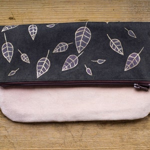 Cartera plegable de inspiración natural en marrón y rosa con hojas pintadas a mano, materiales naturales y detalles metálicos dorados.