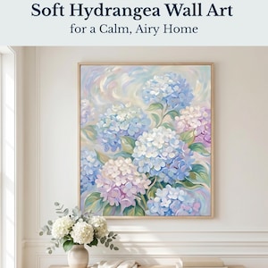 May include: Soft Hydrangea Wall Art for a Calm, Airy Home. A framed painting features a close-up of blue, white, and lavender hydrangeas. The artwork is in a light wooden frame. A vase of white flowers sits on a wooden table.