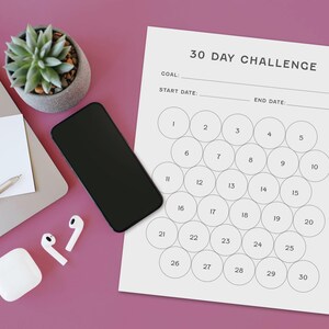 May include: A workspace scene featuring a laptop, smartphone, and a 30-day challenge tracker. The tracker has numbered circles for daily progress. A succulent plant, pen, sticky note, and wireless earbuds are also present on the pink surface.