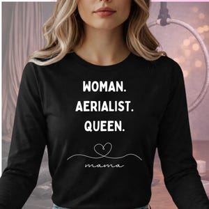 Op de afbeelding: Zwart shirt met lange mouwen en de witte tekst "WOMAN. AERIALIST. QUEEN.". Daaronder een hartvormig ontwerp en het woord "mama" in sierlijke letters. Het shirt heeft een ronde hals.