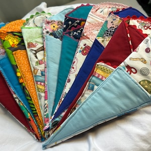 Puede incluir: Una colección de artículos de tela hechos a mano en forma de cono, de colores, abanicados sobre una superficie blanca. Cada cono presenta una tela estampada única, con colores como azul, rojo, naranja y verde. Algunos tienen adornos decorativos.