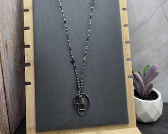 May include: A black beaded lanyard necklace with star accents and a metal clasp. The necklace is displayed on a black background, mounted on a wooden display stand. A small succulent plant in a white pot is in the background.