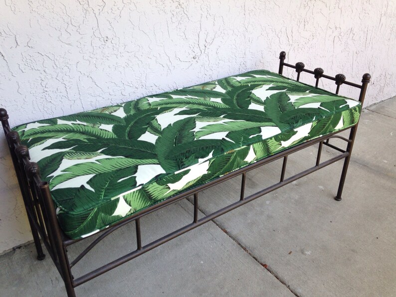 May include: A metal bench with a cushion featuring a green and white tropical leaf pattern. The bench has a dark brown metal frame with decorative finials on the backrest. The bench is approximately 48 inches long.