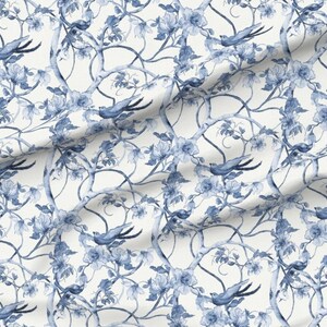 Peut inclure: Un tissu avec un motif r&eacute;p&eacute;titif d'oiseaux bleus, de fleurs et de branches sur fond blanc. Le motif a un effet aquarelle, avec des ombres douces et des d&eacute;tails d&eacute;licats. Les oiseaux sont en vol et les fleurs sont en fleurs.