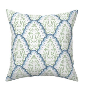 May include: A white throw pillow with a blue and green floral pattern. The pattern features a repeating design of stylized flowers and leaves within a scalloped border.