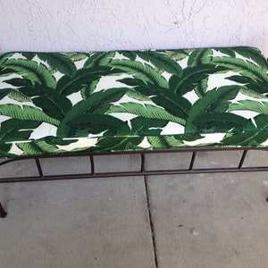 May include: A decorative bench with a metal frame and a cushioned seat. The seat features a vibrant green and white tropical leaf pattern. The metal frame has a dark brown finish.
