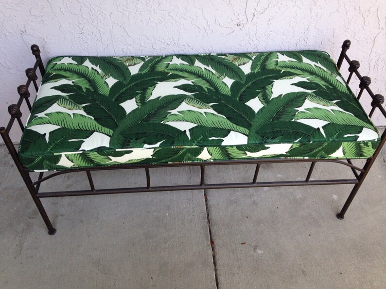 May include: A decorative bench with a metal frame and a cushioned seat. The seat features a vibrant green and white tropical leaf pattern. The metal frame has a dark brown finish.