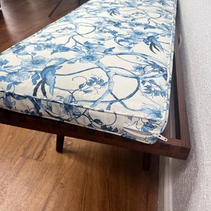 Peut inclure: Banc en bois long avec un coussin orn&eacute; d'un motif floral et d'oiseaux bleu et blanc. Le banc a un cadre et des pieds marron fonc&eacute;. Le coussin a une fermeture &eacute;clair sur le bord.