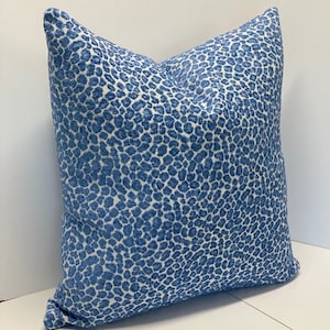 May include: A square decorative pillow with a blue and white animal print pattern. The pillow has a soft, textured appearance and is placed on a white surface. The pillow is designed for home decor.