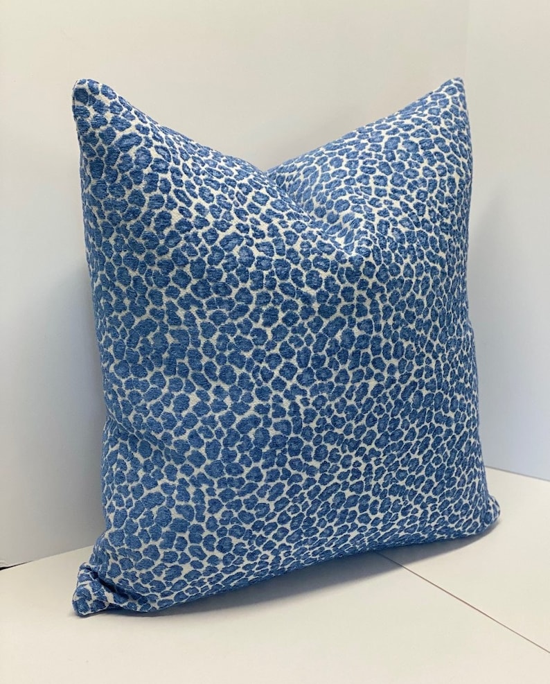 May include: A square decorative pillow with a blue and white animal print pattern. The pillow has a soft, textured appearance and is placed on a white surface. The pillow is designed for home decor.