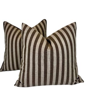 May include: Two brown and beige striped throw pillows. The pillows are made of a soft, woven fabric and have a subtle sheen.
