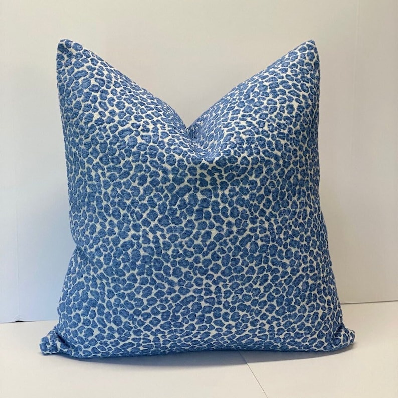 May include: A square decorative pillow with a blue and white leopard print pattern. The pillow has a textured appearance and is filled, creating a plump, inviting shape. The pillow is a home decor item.
