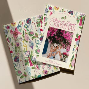 May include: Christmas cards with a festive design. One card features a family photo framed by the words "Merry & Bright Christmas." The other card has a pattern of ornaments, candy canes, and holly. The cards are cream-colored with pink and green accents.