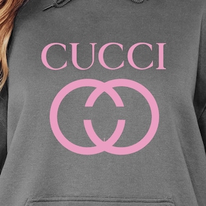 Puede incluir: Sudadera gris con el texto "CUCCI" en rosa y un diseño de doble círculo rosa. La sudadera tiene una capucha con cordón y un bolsillo delantero. El diseño está centrado.