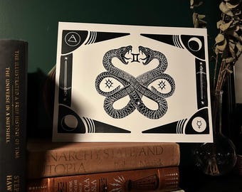 May include: Black and white art print featuring two intertwined snakes facing each other. The print has geometric border elements with symbols. The print is displayed on a shelf with several books, including "The Illustrated A Brief History of Time".