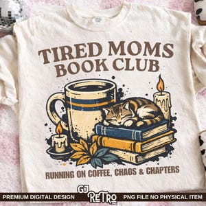Può includere: T-shirt color crema con grafica retrò. Il design include una tazza di caffè, un gatto che dorme sui libri e candele. Il testo recita "TIRED MOMS BOOK CLUB" e "RUNNING ON COFFEE, CHAOS & CHAPTERS".