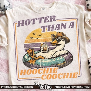 Puede incluir: Camiseta color crema con un diseño retro de un pato con gafas de sol y sombrero de vaquero, flotando en una boya y sosteniendo una bebida. El texto dice "HOTTER THAN A HOOCHIE COOCHIE" en naranja y morado.