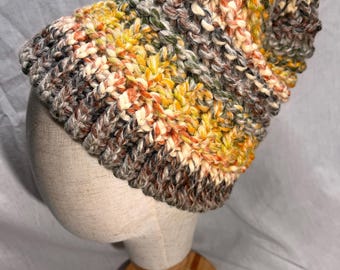 May include: A handmade, multi-colored knit beanie hat. The hat features a mix of colors including yellow, orange, green, brown, and gray. The hat is displayed on a mannequin head.