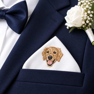 May include: A white pocket square featuring a detailed golden retriever embroidery, tucked into the breast pocket of a navy blue suit jacket. A matching navy blue bow tie and a white rose boutonniere with baby's breath are also visible.