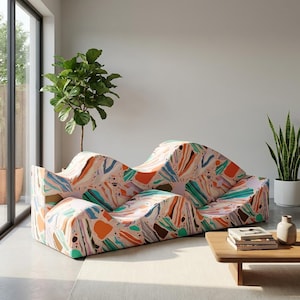 May include: A contemporary, undulating sofa featuring a vibrant abstract design in pink, orange, blue, and green. The sofa is set in a well-lit room, complemented by a wooden coffee table and potted plants.