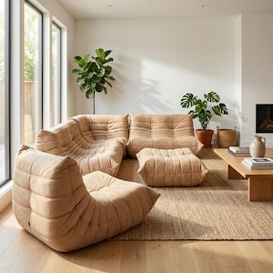May include: A contemporary living room with a beige sectional sofa, an armchair, and an ottoman. The furniture has a textured, quilted design. The room includes a wooden coffee table, plants, and a woven rug, creating a comfortable and stylish space.