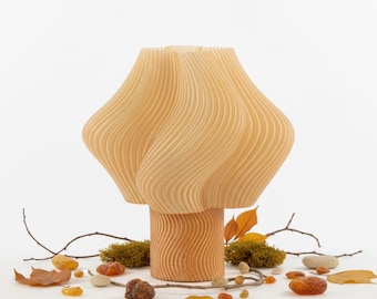 May include: A wooden mushroom-shaped lamp with a wavy design. The lamp is light brown and sits on a light brown base. The lamp is surrounded by leaves, small rocks, and twigs.