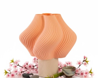 May include: A peach-colored, abstract vase with a textured, ribbed design. The vase sits atop a cream-colored base. Cherry blossoms, small stones, a bamboo stalk, and a small ceramic cup surround the vase, creating a serene, decorative display.