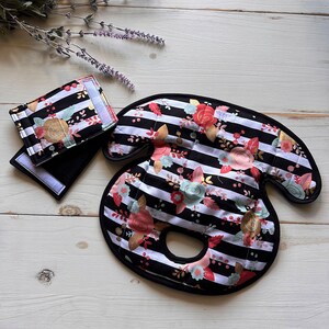 May include: Black and white striped fabric car seat headrest with a floral pattern in pink, gold, and green. The headrest has a hole in the center for a child's head.