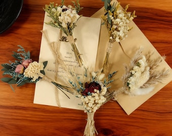 May include: A collection of small, dried flower bouquets tied with twine, arranged on a wooden surface with beige stationery. The bouquets feature a variety of colors, including white, red, and green, creating a rustic and natural aesthetic.