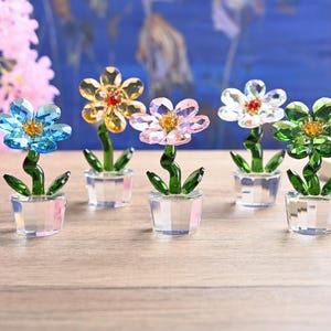May include: Six crystal flower ornaments in shades of blue, yellow, pink, white, and green. Each flower has a clear crystal pot, green stem, and leaves. The flowers are displayed on a wooden surface.
