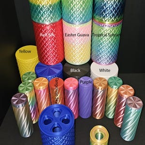 May include: A collection of colorful, cylindrical containers with diamond-patterned exteriors. The containers are in various colors, including yellow, red, blue, and purple, with some displaying gradient color schemes. Some containers have the text "Tropical Sunrise", "Tropical Sunrise 2", "Pineapple Ocean", "Easter Guava", "Tropical Sunset", "Tangerine Sky", "Blue Silk", "Black", "White", and "Yellow".