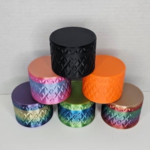 May include: A collection of six cylindrical containers arranged in a pyramid formation. Each container features a textured diamond pattern on the sides and a smooth flat lid. The colors include solid black, bright orange, and various gradients.