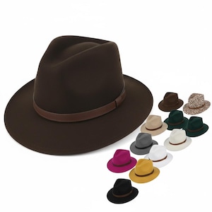 Può includere: Un cappello fedora marrone scuro con una fascia in pelle marrone. Sullo sfondo sono esposti diversi altri cappelli fedora in vari colori, tra cui nero, grigio, bianco, giallo e rosa. I cappelli hanno un design classico ed elegante.