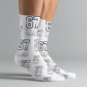 May include: White socks with a repeating pattern of the number "67" and the word "seven" in black. The design also includes hand gestures. The socks are worn on a person's feet.