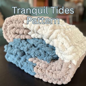 May include: A folded, chunky knit blanket in shades of blue, white, and tan. The blanket is made of a soft, plush material. The text "Tranquil Tides Pattern" is displayed in white, centered at the top of the image.